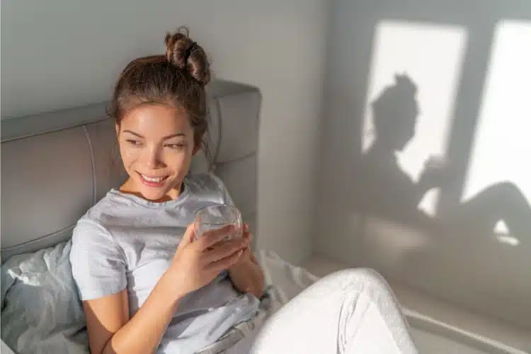 Woman drinking a glass of water feeling happy after waking up with pain relief in her body.